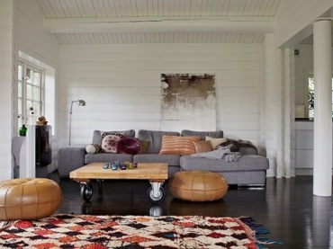 Tkane dywany berberyjskie w etnicznych wzorach,marokańskie skórzane pufy,stolik z palety na kółkach i szara sofa w salonie (24897)