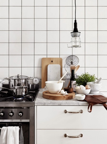 Biała kwadratowa glazura na ścianie w kuchni,industrialna lampa wisząca,drewniane deski deserowe w białej kuchni
