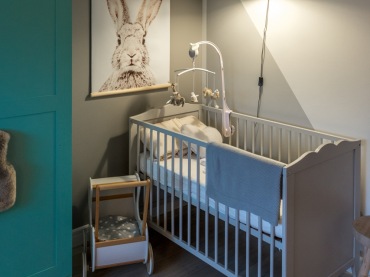 Obok niebieskiej szafy, w rogu pomieszczenia znalazło się małe łóżeczko dla niemowlęcia. Ta część pokoiku dziecięcego...