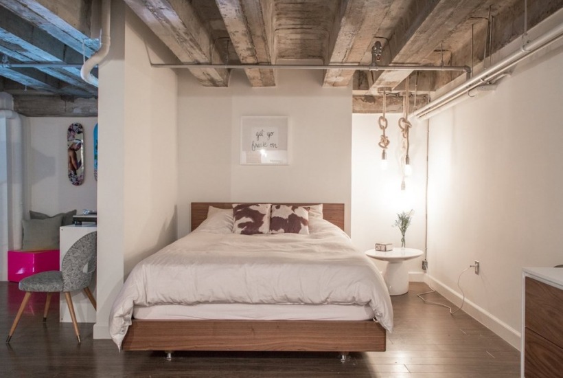 Drewniane nowoczesne łóżko w białej sypialni w lofcie z żarówkami na grubym powrozie