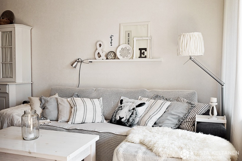 Biało-szary salon w stylu skandynawskim,poduszki w graficzne wzory i druki,dekoracja półki nad sofą