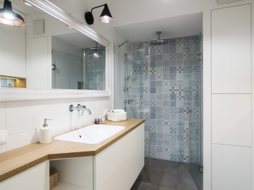 Aranżacja całkiem przestronnej łazienki w stylu skandynawskim, gdzie dominuje biel i drewno. Wzorzysta ściana w części...
