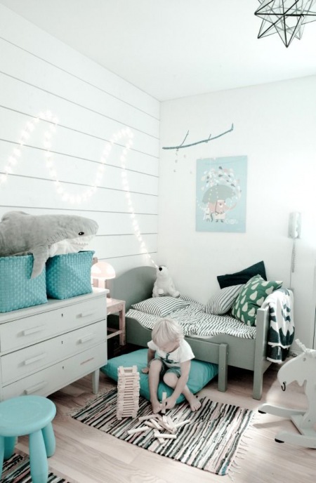 Turkusowe poduszki, kosze i plakaty w białym pokoju dla dziecka