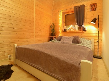 W drewnianej sypialni znajduje się podwójne łóżko oraz regalik pełniący funkcję stolika nocnego. Poza stojącą lampą są...