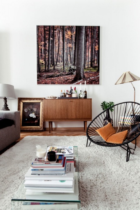 Biały futrzany dywan,ażurowy okragły fotel,obrazy i brązowa komoda z lat 60-tych w białym salonie w stylu eklektycznym