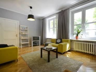 Bardzo duży i wysoki salon urządzono w prostym skandynawskim stylu. Wnętrze zdecydowanie dekorują żółte fotele, poza tym dekoracje są zastosowane w oszczędnej formie. Biały regalik pod ścianą w formie drabiny podkreśla klimat pokoju...