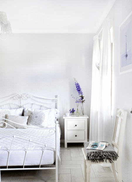 Białe kute łóżko w aranżacji sypialni z bielona podłogą z desek