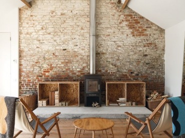rustykalny salon, ale w nowoczesnym wydaniu - w tle ściana z czerwonej cegły,proste, drewniane meble oraz żeliwny, czarny kominek o prostej...