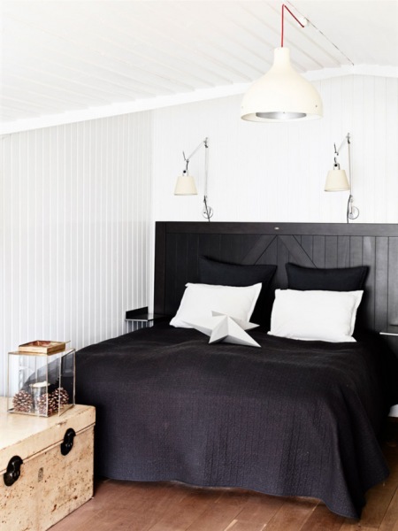 Czarne drewniane łóżko,czarna narzuta,drewniana skrzynia vintage i białe lampy i kinkiety w białej sypialni