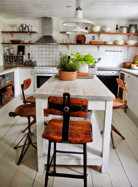 Industrialne krzesła w stylu vintage w aranżacj białej kuchni z drewnianymi pólkami i białym postarzanym stołem