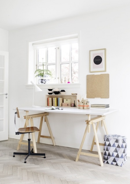Skandynawskie białe biurko na drewnianych kozłach,drewniane nowoczesne krzesło na metalowym krzyżaku i korkowe detale w aranzacji prostego domowego biura,