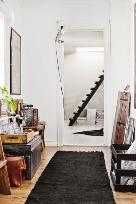 Srebrny kinkiet nowoczesny,czarny tkany dywanik,drewniane skrzynki,czarne schody i brązowe walizki vintage