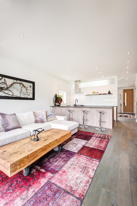 Industrialny drewn iany stolik na kółkach,dywan patchwork i biala sofa w aranzacji otwaetej przestrzeni salonu z kuchnią