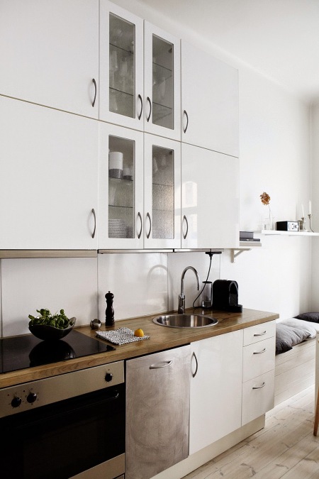 Biała nowoczesna kuchnia z drewnianymi blatami, bieloną podłogą z desek i siedziskami przy ścianie