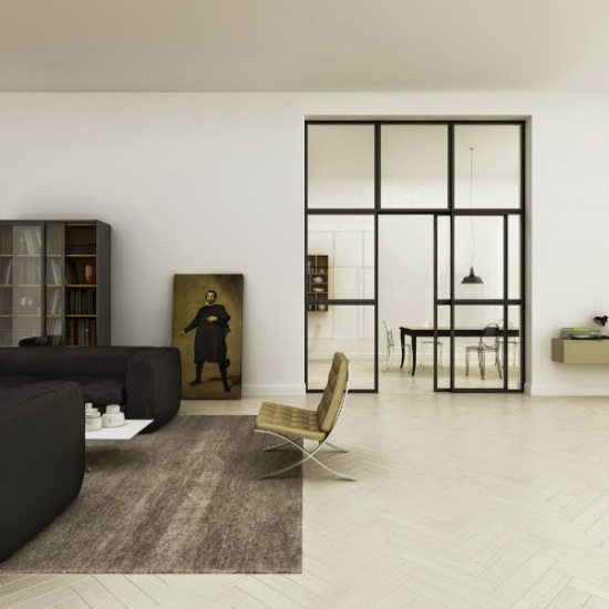 Metalowa i przeszklona ściana z drzwiami w aranzacji salonu z czarnymi sofami,szarym dywanem i miodowo-złotym nowoczesnym fotelem na metalowych nogach płozach
