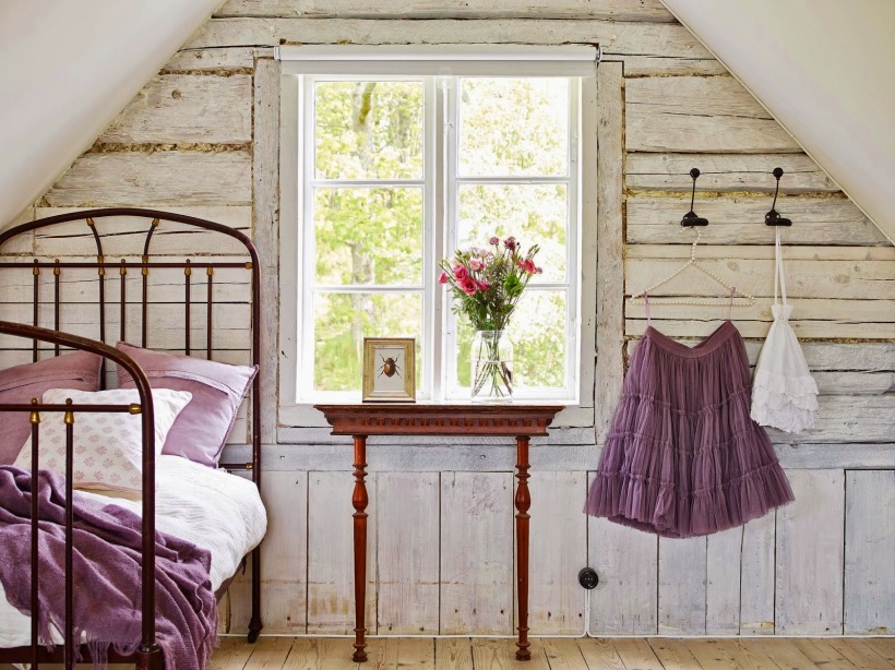 Drewniane przecierane deski na ścianie w sypiani na poddaszu,kute łóżko i stylowa konsolka z drewna przy oknie