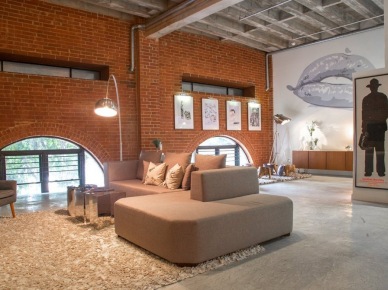 Beżowy nowoczesny narożnik,dizajnerkie stoliki lustrzane yes,lampa podłogowa z wysięgnikiem ,betonowa podłoga i ściana z czerwonej cegły w salonie (26727)
