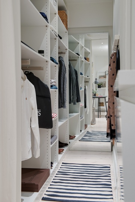 Biała zabudowa szafy z otwartymi półkami w wąskiej i małej garderobie