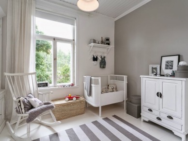 Biały fotel na płozach,biała komoda i łóżeczko w skandynawskiej aranżacji pokoju dla dziecka,szara śćiana i dywan w szaro-białe paski (47927)