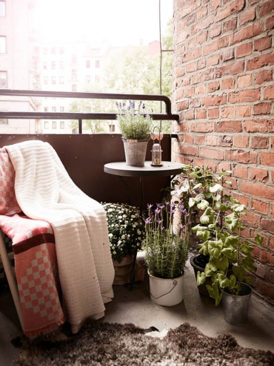 Mały balkon z fotelem,okrągłym stolikiem,roslinami w doniczkach i czerwoną cegłą na ścianie