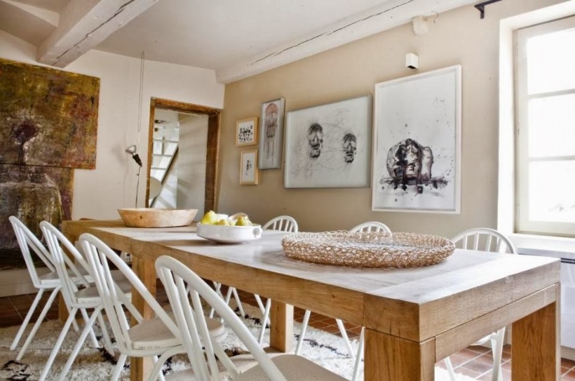 Prosty rustykalny stół z naturalnego drewna,białe skandynawskie krzesła,nowoczesne grafiki na scianach w jadalni z bielonymi belkami z drewna