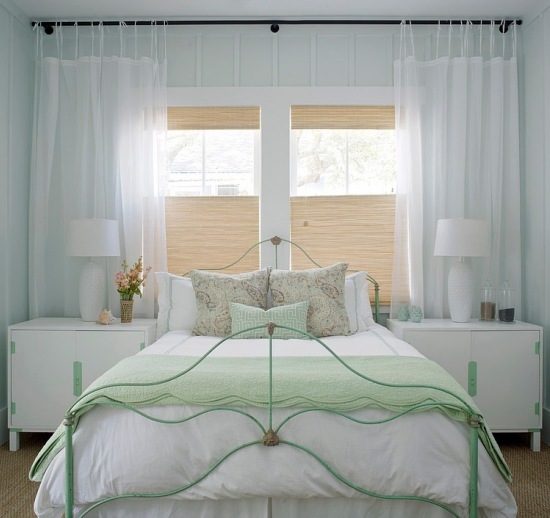 Białe firany na troczkach i kute łóżko w mietowym kolorze w sypialni