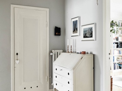 Biało-szara aranżacja małego przedpokoju ze stylową biała komodą z szufladami,podłogą z drewnianych desek i skandynawskim dywanikiem (27038)