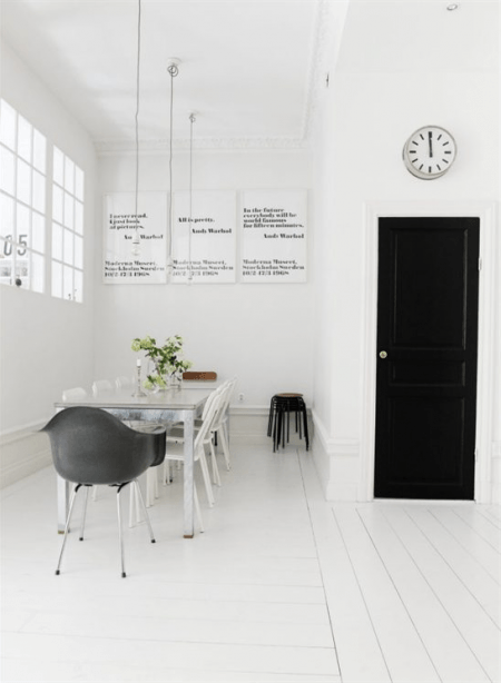 Aranżacja białej jadalni skandynawskiej z białą podłogą, ścianami i czarnymi drzwiami