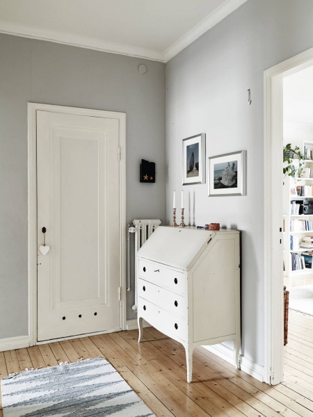 Biało-szara aranżacja małego przedpokoju ze stylową biała komodą z szufladami,podłogą z drewnianych desek i skandynawskim dywanikiem