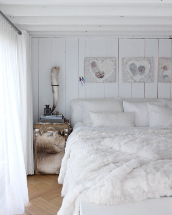 Dekoracyjne serca w białej sypialni z futrzaną narzutą, drewnianą podłogą i szafką kufrem w beżowo-białym futerku