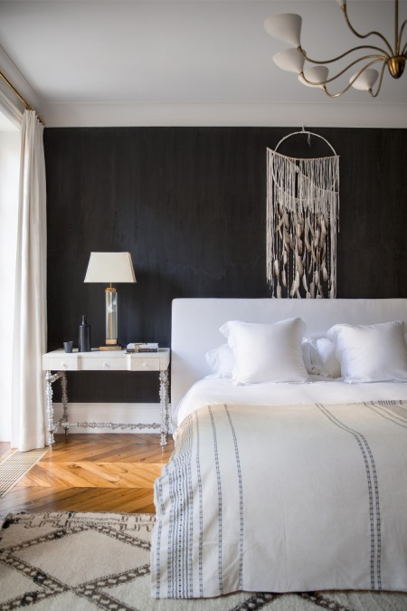 Białe łóżko tapicerowane przy czarnej ścianie w skandynawskiej sypialni z klasycznymi dodatkami