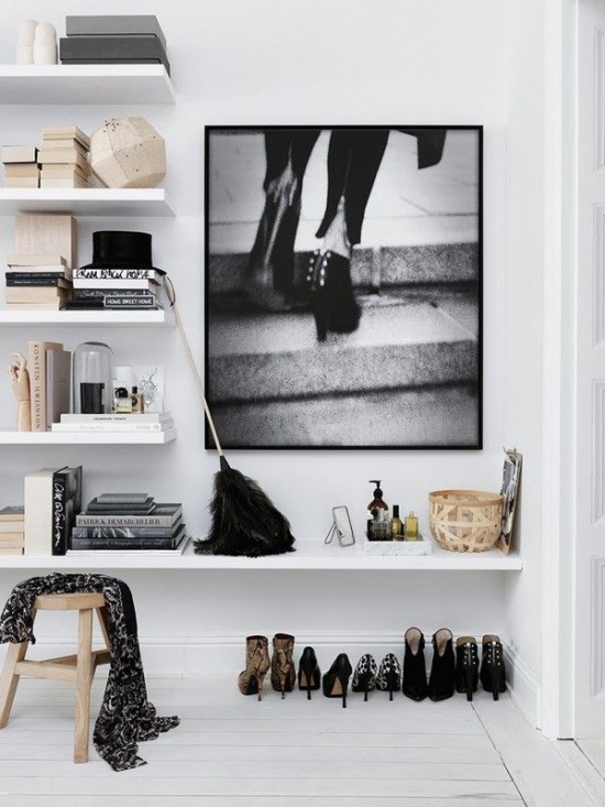 Białe malowane deski na podłodze,białe półki na scianie,drewniany stołek i biało-czarna fotografia na ścianie w przedpokoju