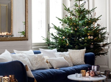 Granatowa sofa z białymi poduszkami dekoracyjnymi, okragły stolik kawowy i świateczna choinka w salonie (27546)