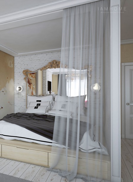 Łóżko na drewnianym podeście z szufladami we wnęce w otwartym salonie ze ścianą z białej cegły i barokowym dużym lustrem nad wezgłowiem łóżka