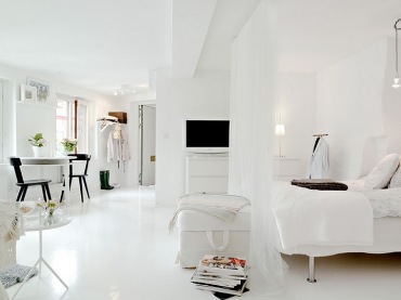 białe mieszkanie, w którym na jednej przestrzeni znalazły się kuchnia z sypialnią i salon z jadalnią - dobry pomysł na...