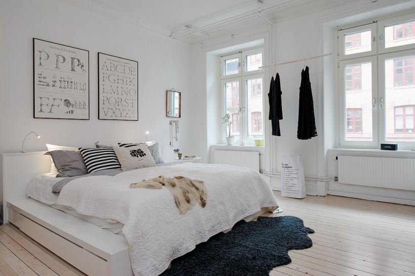 Biała sypialnia skandynawska z typografiami na ścianie i szarym futrzakiem na drewnianej podłodze