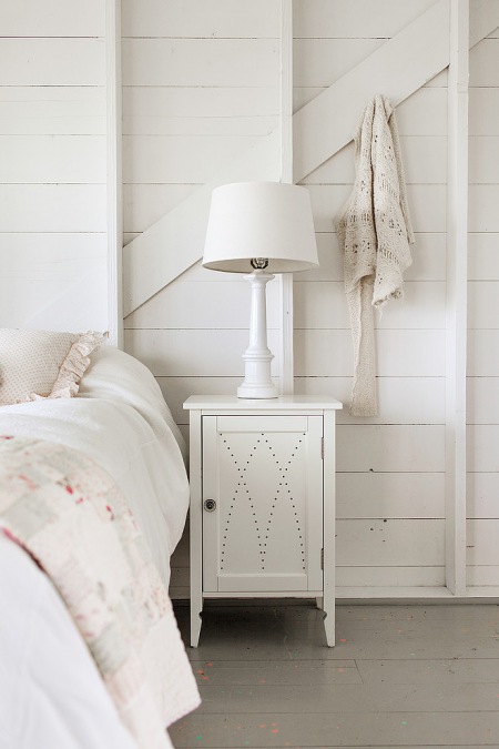 Aranżacja białej sypialni ze ścianasmi z białych desek i szarą podłogą