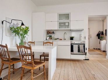 Biala kuchnia w nowoczesnymstylu, gdzie drewniane krzesla i podloga dodaja jej skandynawskiego charakteru.