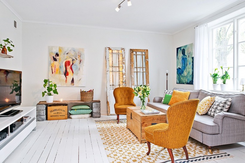 Ciemnożółte fotele i poduszki,drewniane skrzynki,nowoczesne obrazy i skandynawski dywan w aranżacji salonu