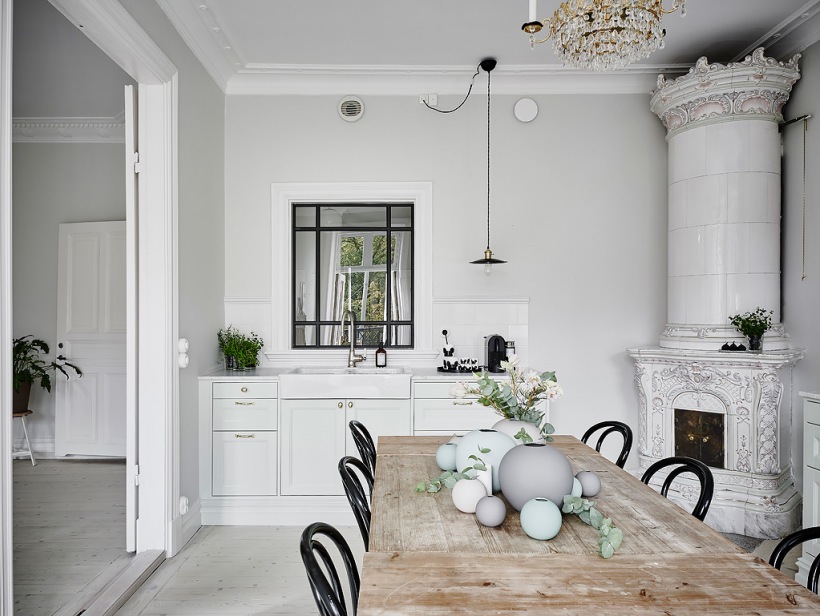 Wewnętrzne metalowe okno w małej kuchni z ceramicznym piecem skandynawskim,postarzany bielony stół z drewna z czarnymi gietymi krzesłami