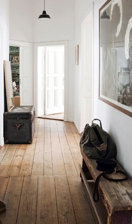 Czarny kufer kolonialny,drewniana wiejska ławka,drewniane deski na podłodze  i duża czarno-biała fotografia na białej ścianie w przedpokoju