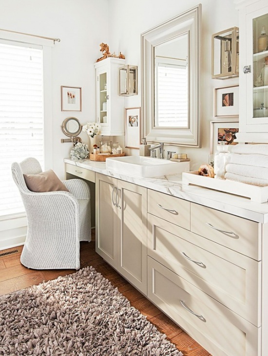 Biała łazienka w tradycyjnej aranżacji z wiklinowym fotelem,drewnianym lustrem,drewnianą podłogą z desek i zabudową szafek z umywalką naszafkową