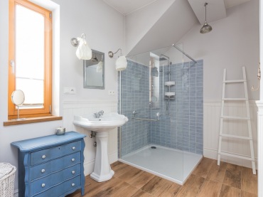 Wygodna łazienka z dużą kabiną prysznicową oraz białą oryginalną umywalką. Chłodne kolory bieli i błękitu ocieplają...
