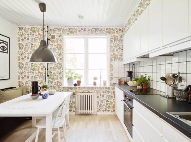 Kolorowa  kwiatowa tapeta na ścianie w białej kuchni skandynawskiej z szarą lampą i drewnianą podłogą (24920)