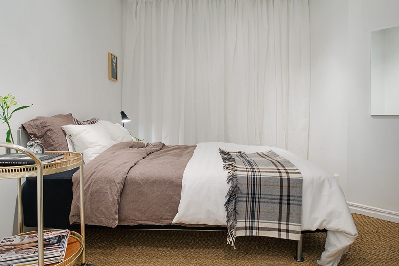 Białe zasłony,beżowa pościel i kraciastay pled w aranżacji skandynawskiej sypialni