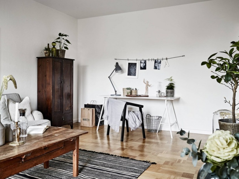 Kącik biurowy z białym biurkiem i czarnym krzesłem,drewniany rustykalny stolik kawowy,tkany dywan,szafa rustykalna w brązowym kolorze drewna w salonie