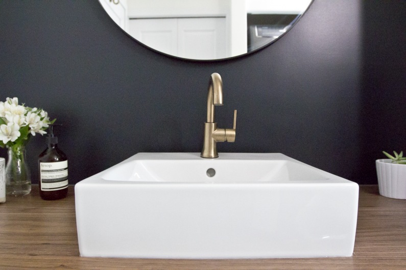 Wyjątkowy szyk nadaje łazience złoty kran. Również tworzy spory kontrast z ciemną ścianą