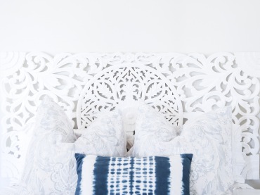 Białe, dekoracyjne wezgłowie stanowi w tej sypialni niezwykłą ozdobę. Białe tło ściany i jasne poduszki wprowadzają do...