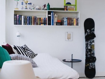 Pokój dla nastolatka urządzono w minimalistycznym stylu. We wnętrzu znajduje się pasiaste łóżko oraz półka na książki....