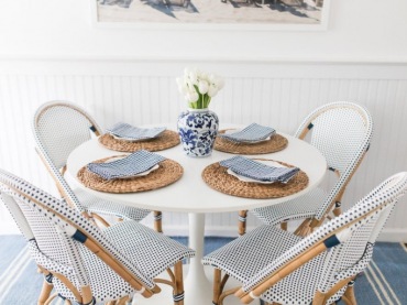 Drewniane nogi i ramy krzeseł z wyplatanymi siedziskami i wiązaniami w niebieskim kolorze zdobią jadalnię, nadając jej...